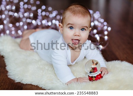 Very cute baby lying on the floor on the background lights near the Christmas ball and smiling