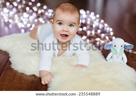 Very cute baby lying on the floor on the background of Christmas lights next to the soft toy and smiles
