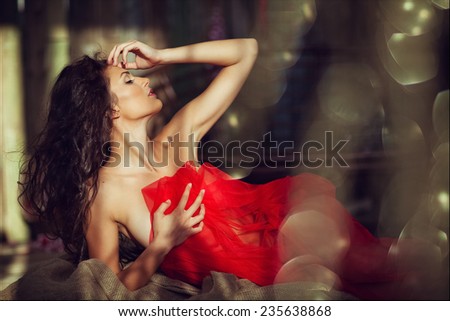 Sexy sensual very beautiful curly girl in a red dress lying on linen fabric