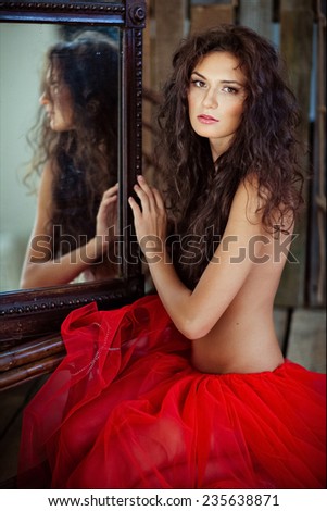 Sexy sensual very beautiful curly girl in red skirt sitting near mirror