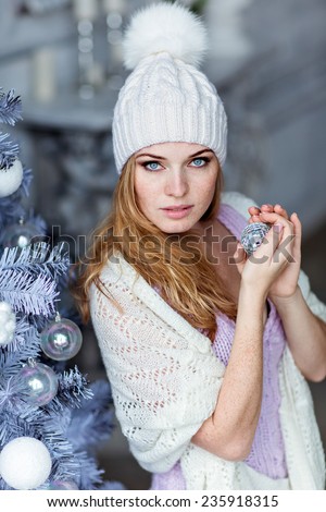 Very beautiful red-haired girl with blue eyes in a white hat costs about silver Christmas tree