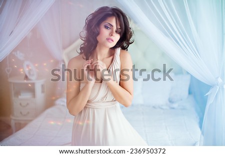 Portrait of a gentle sensual girls brunette sitting on a white bed in a beige dress