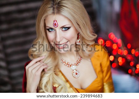 Beautiful and sensual blonde girl in Indian red saree on the background of red lights, close up