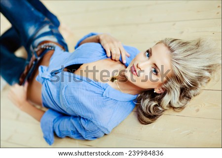 very beautiful, sensual sexy blonde girl with blue eyes in a blue blouse lying on the floor