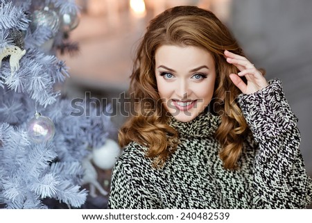 Very beautiful and sensual blonde girl in a knitted sweater smiles on the background of the Christmas tree, close up