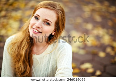 portrait of a beautiful and smiling redhead girl with freckles on the autumn landscape