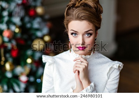 Portrait of a beautiful blonde girl in a white blouse in the background of Christmas lights