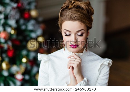 Portrait of a beautiful blonde girl in a white blouse with her eyes closed against the background of Christmas lights