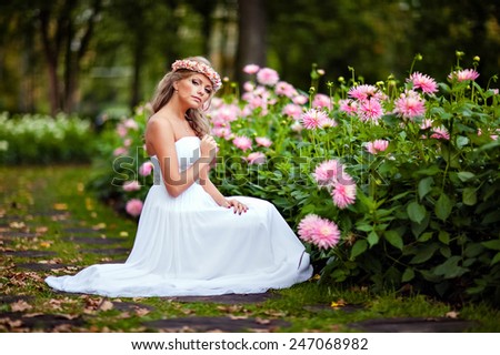 Portrait of a beautiful bride with a diadem of flowers on his head and in a white dress against the background of the autumn flowers