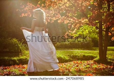 A tender portrait of a beautiful bride with a diadem of flowers on his head and in a white dress against the background of the autumn landscape