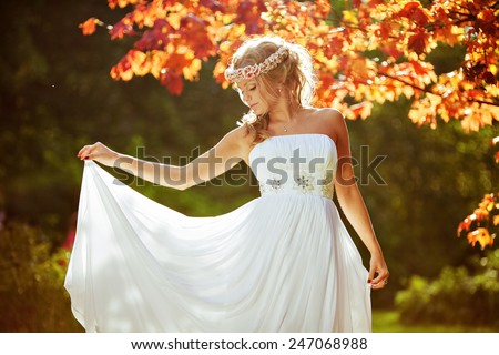 delicate beautiful bride with a diadem of flowers on his head and in a white dress against the background of the autumn landscape