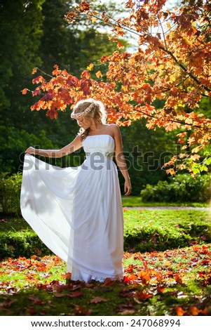 Portrait of a beautiful bride with a diadem of flowers on his head and in a white dress against the background of the autumn landscape