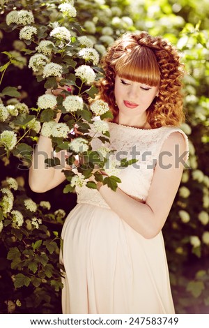 Beautiful red-haired and curly-pregnant girl with her eyes closed, against the green bushes