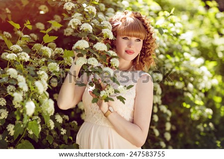 Beautiful red-haired and curly pregnant girl looks against the green bushes