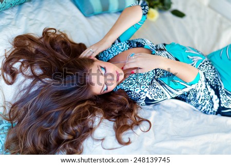 portrait of a very beautiful pregnant girl with gorgeous brown hair and eyes closed in a blue dress lying on the bed