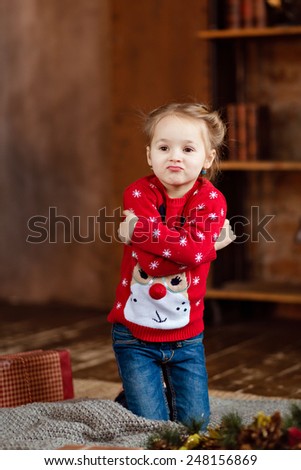 Little girl kid in the red sweater makes faces at Christmas background