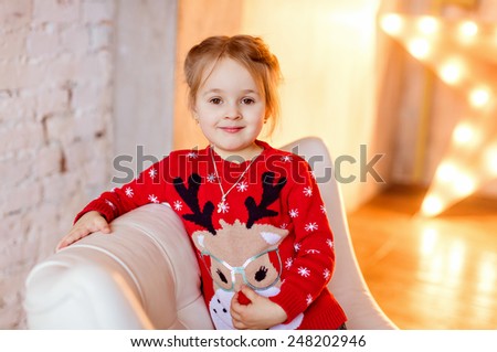 Little girl child with brown eyes smiles in the red sweater on the background of yellow lights