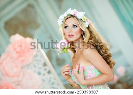Very beautiful blonde girl in a lace dress with a wreath of flowers on his head, looks at the background of spring pink flowers