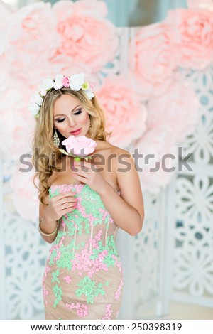 Very beautiful blonde girl in a lace dress with a wreath of flowers on his head, looks at the flower, on the background of spring pink flowers