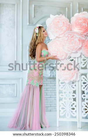 Very beautiful sensual girl with curly blond hair and a wreath of delicate spring flowers, is on the background of large pink flowers, in full growth