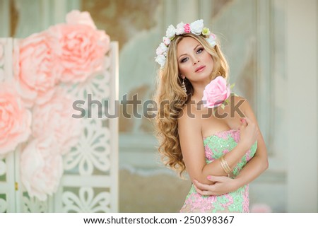 Very beautiful blonde girl in a lace dress with a wreath of flowers on his head, holding a flower, on the background of spring pink flowers
