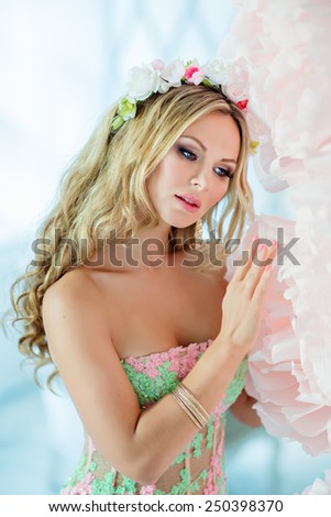 Very beautiful sensual girl with curly blond hair and a wreath of delicate spring flowers, on the background of large pink flowers