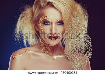 Portrait of a glamorous blonde girl with beautiful Golden makeup and gold foil on dark blue background in Studio, close-up