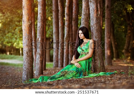 Sexy sensual very beautiful brunette girl with long hair in a green dress sitting in trees