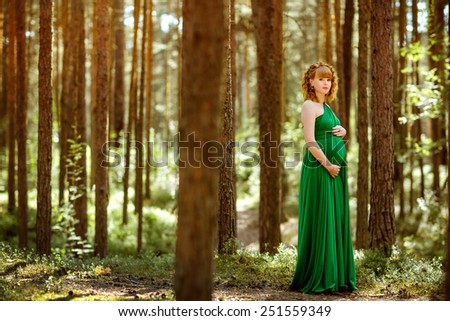 Portrait of a beautiful curly haired pregnant girl in the green dress in the woods among the pines