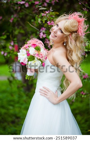 Very beautiful happy bride blonde curly hair in a white dress and delicate unusual bouquet in hand, against the background of Apple blossoms