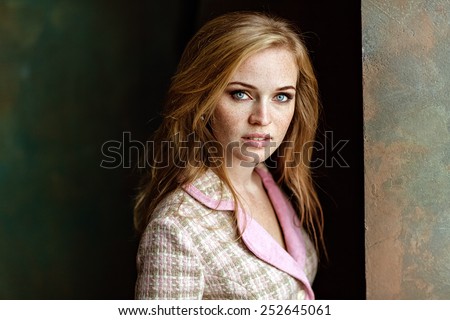 Portrait of sensual very beautiful redheaded girl with freckles in pink tweed suit, standing near the wall, close up