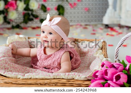 Small very cute, big-eyed little girl in a pink dress lying in a wicker basket about pink tulips