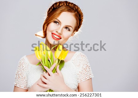 Beautiful girl with red hair in a braid, holds yellow tulips with closed eyes on white background in Studio