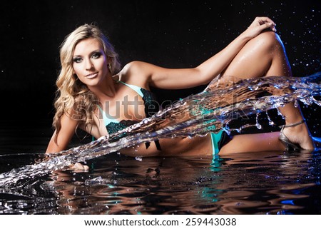 Very beautiful sexy girl blonde in black and blue swimsuit on the background of flowing water and water spray in the Studio on a dark background
