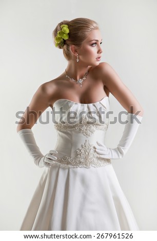 Portrait of beautiful delicate blonde bride in wedding dress with green and flowers in her hair on white background in Studio profile