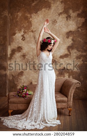 Portrait of beautiful sensual brunette girl in a white lace dress, with a wreath of flowers on her head, in full growth on a brown background in the Studio