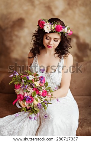 Portrait of beautiful sensual girls brunette  in white lace dress, with a wreath of flowers on his head, sitting on the couch and looking down
