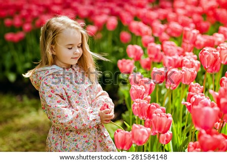 portrait of a very cute pretty girls blonde in a pink cloak with eyes closed around the flower bed of red tulips in the Park