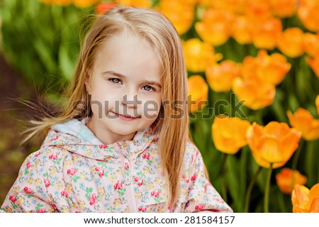 portrait of a very cute pretty girls blonde in a pink cloak around flower beds with red tulips in the Park