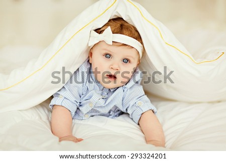 Portrait of a little girl baby with blue eyes in a striped blue blouse lying on the bed under a white blanket