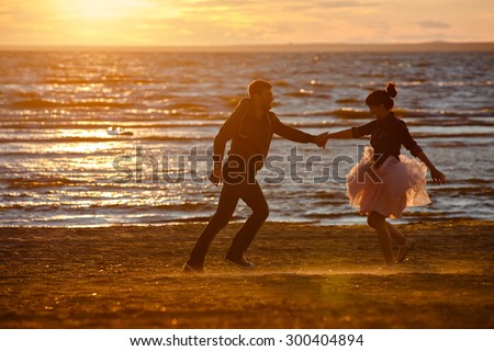 Silhouettes of men and women in the lush short skirt, running across the sand and smiling on the background of the sea and the Golden sunset
