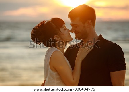A man and a woman in a lush short skirt, looking at each other tenderly and smiling on the background of the sea and the Golden sunset