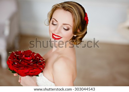 Portrait of a charming girl blonde with beautiful smile and red lipstick, with her eyes closed ,with a bouquet of red roses on the background of the interior, close-up