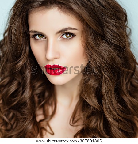 Portrait of a beautiful glamorous brunette with curly hair and bright makeup with red lipstick, close-up, beauty
