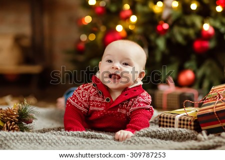 Little boy the kid in the red sweater lying on a cozy blanket on the Christmas tree and garlands in the house next to the gifts
