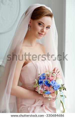 Gentle, sensual portrait of very beautiful girls bride blonde in a pink dress and veil with a bouquet of flowers in his hands, a bright interior