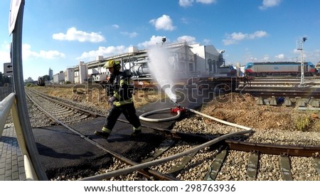 HAIFA, ISRAEL - JUNE 30, 2015: Firefighters from Northern Israel with protective gear during simulation drill of leak of Bromine chemical in a container car of train. Water stream is applied.