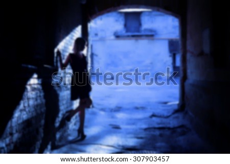 The silhouette of a woman in a black alley (blurred background)