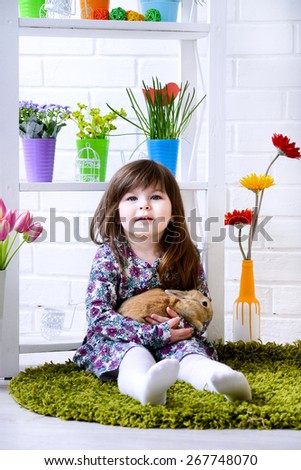 Little girl holding a fluffy rabbit with flowers around. Easter Spring concept