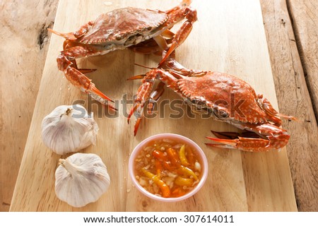 Two boiled crabs on wooden cutting board with seafood sauce.